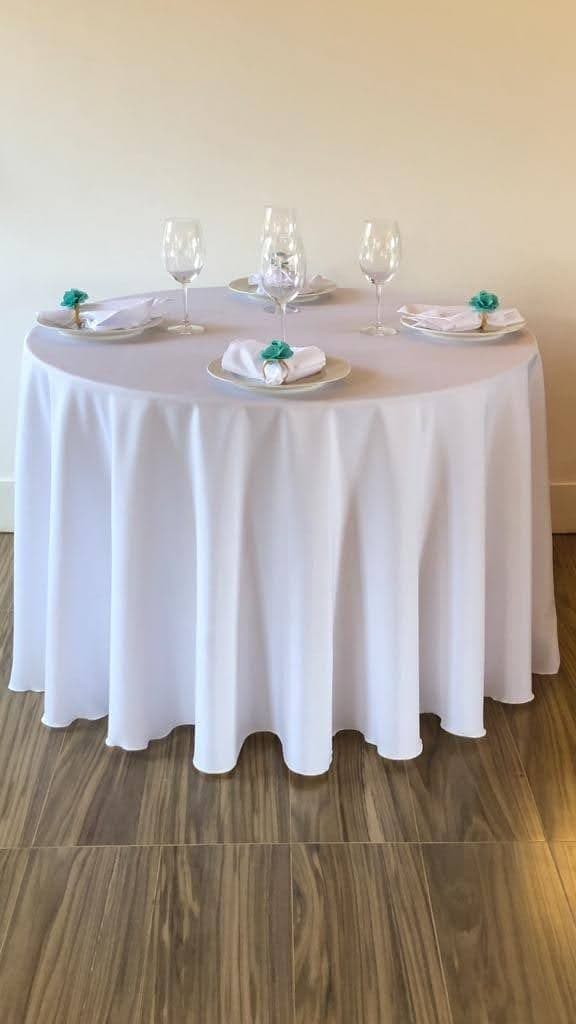 Mesa redonda com toalha branca longa e arranjo formal para quatro lugares